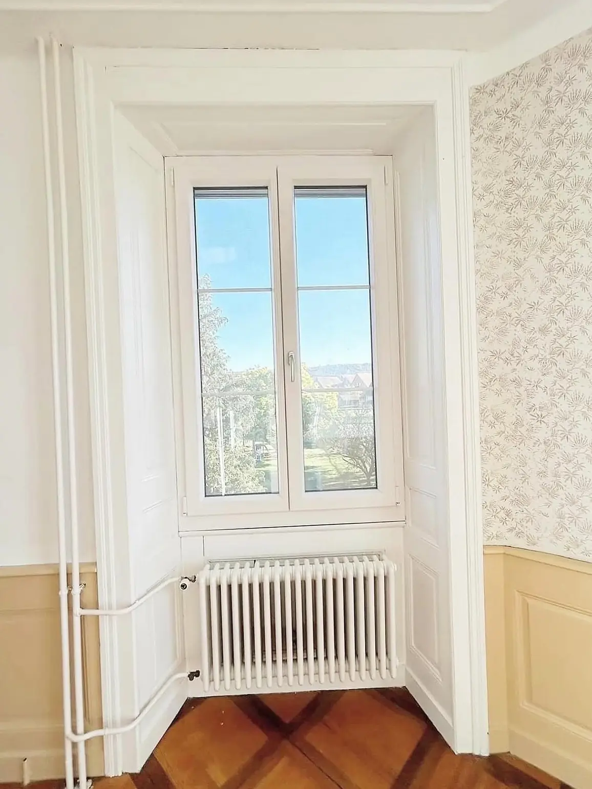 Fenêtre à deux battants et radiateur devant un soubassement beige